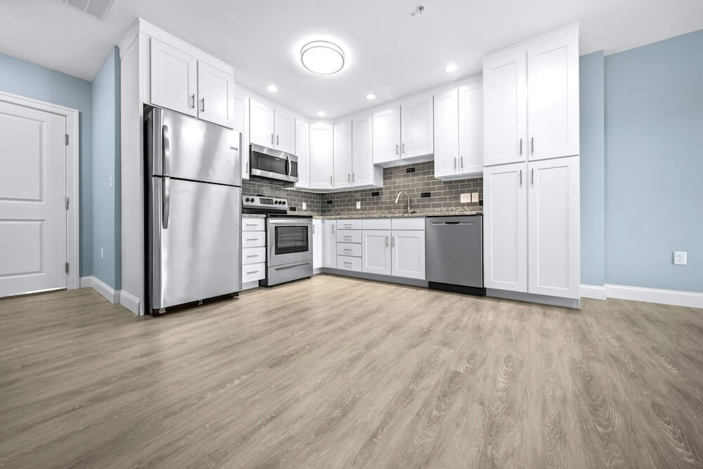 A pristine kitchen featuring white cabinets, stainless steel appliances, and sound-absorbing modular acoustic flooring.