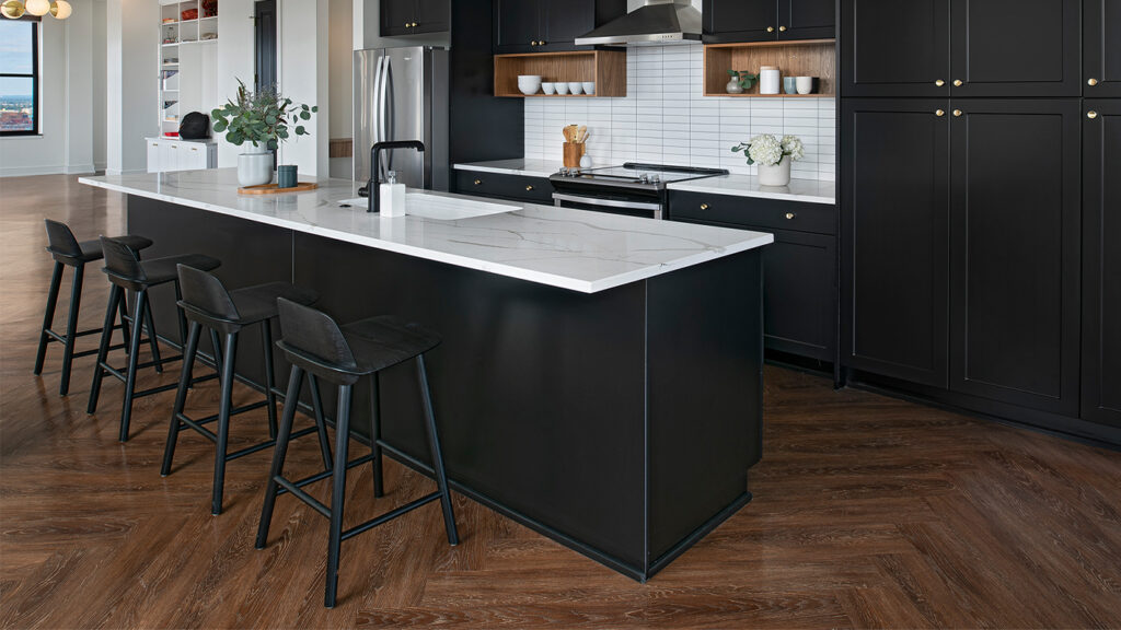 A kitchen area featuring black cabinets and a black bar with white marble counter tops, black bar stools, and dark brown wood look LVT flooring.
