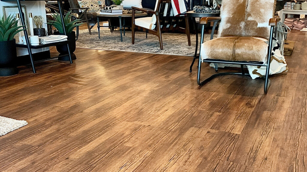 A multifamily housing complex retail space, featuring wood look LVT flooring, a black ceiling, cow-hide armchair, chandelier and various pieces of furniture and home decor.