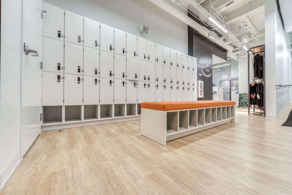 Limed Wood LVT flooring in a modern store interior featuring rows of white lockers, a central bench with shoe cubbies, and clothing racks in the background.