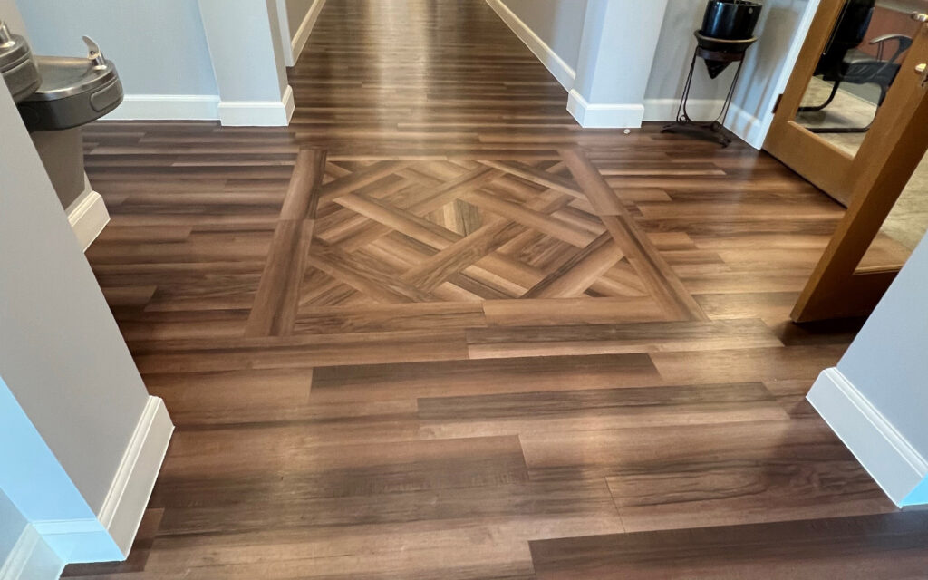 Hallways of a commercial building with wood look luxury vinyl plank running perpendicular and an inset pattern in a crosshatch pattern. 