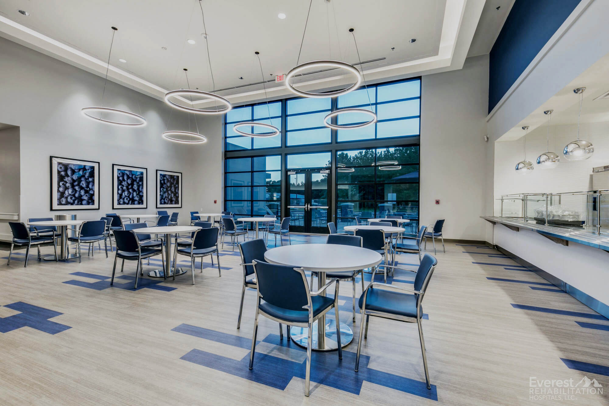A spacious hospital cafeteria with blue and gray-toned luxury vinyl tile from the Spectrum collection, arranged in a guiding pattern beneath round tables and pendant lights.