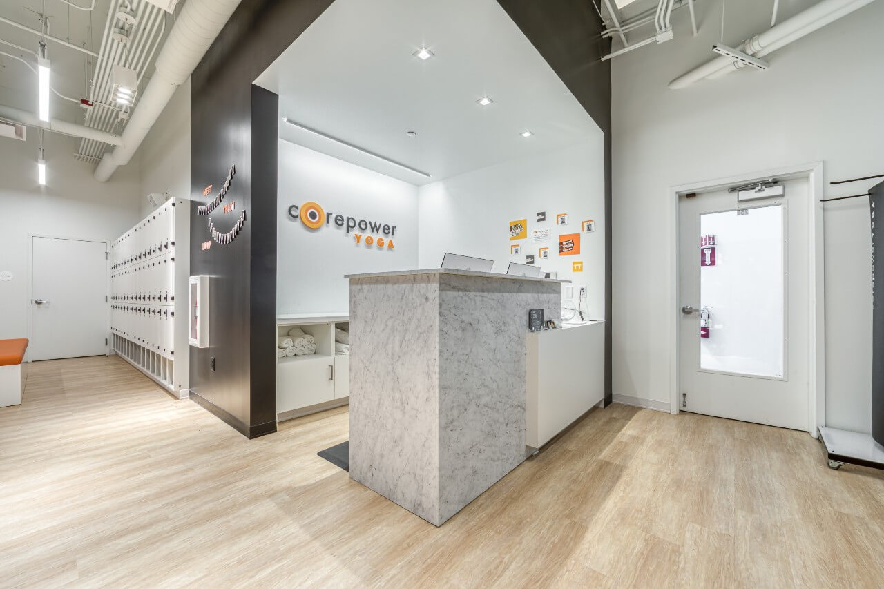 A yoga studio reception with Limed Wood luxury vinyl plank flooring, a marble check-in desk, white shelving, and bright modern decor.
