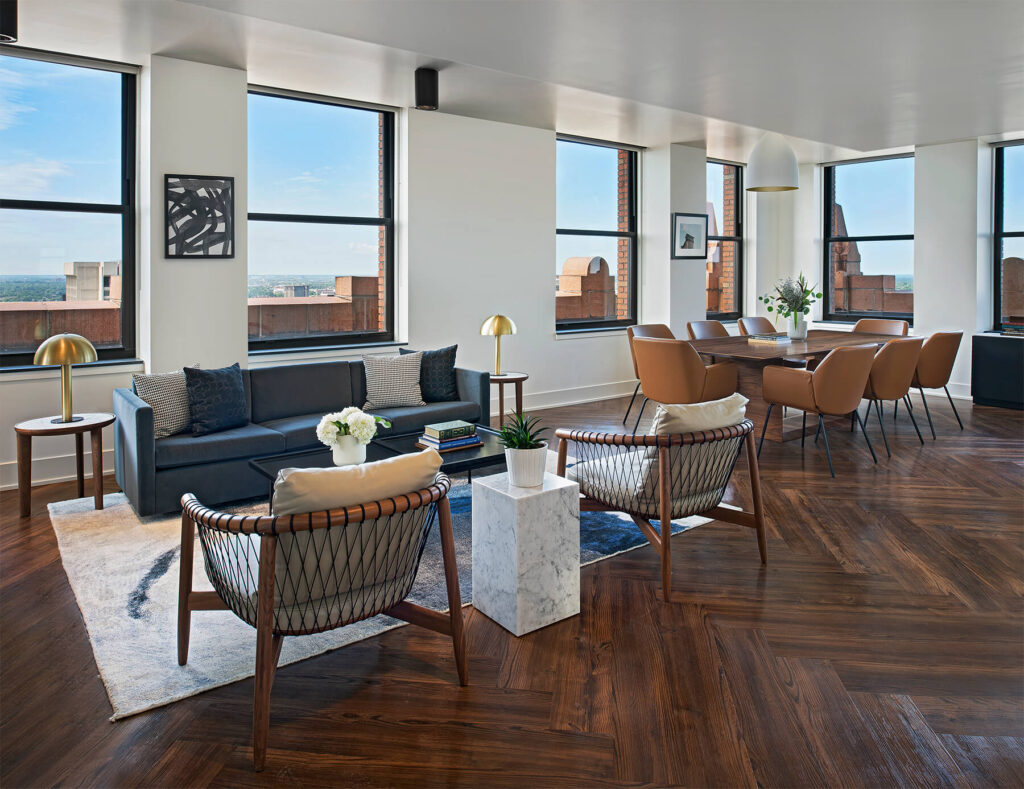 A luxury apartment lounge with custom herringbone-patterned LVT flooring, modern seating, large windows with city views, and mid-century decor accents.